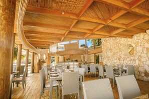 An outdoor dining area with wooden beams, stone walls, and wicker furniture. - Atabey Luxury Paradise (Punta Cana)