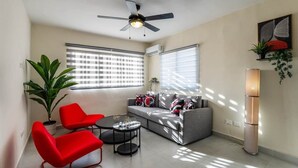 Ein modernes Wohnzimmer mit einem grauen Sofa, roten Sesseln, einem Couchtisch, einem Deckenventilator und einer Stehlampe.