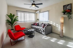 Ein modernes Wohnzimmer mit einem grauen Sofa, roten Sesseln, einem Couchtisch, einem Deckenventilator und einer Stehlampe.