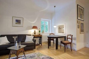 A living room with a sofa, a coffee table, a dining table with chairs, a lamp, and framed pictures on the walls. - Strandvilla Hubertus - H3 - Gustav Klimt (Ostseebad Boltenhagen)
