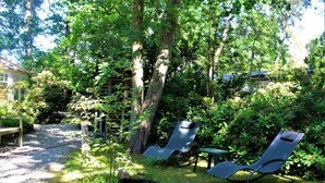 Un jardin avec deux chaises longues et une table, entouré d’arbres et de verdure.