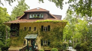 Un grand bâtiment recouvert de lierre, de style architectural traditionnel, avec une entrée imposante et une petite voiture garée devant.