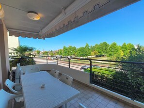 Ein Balkon mit Tisch und Stühlen, einem Geländer und Blick auf eine Straße und Grünflächen.
