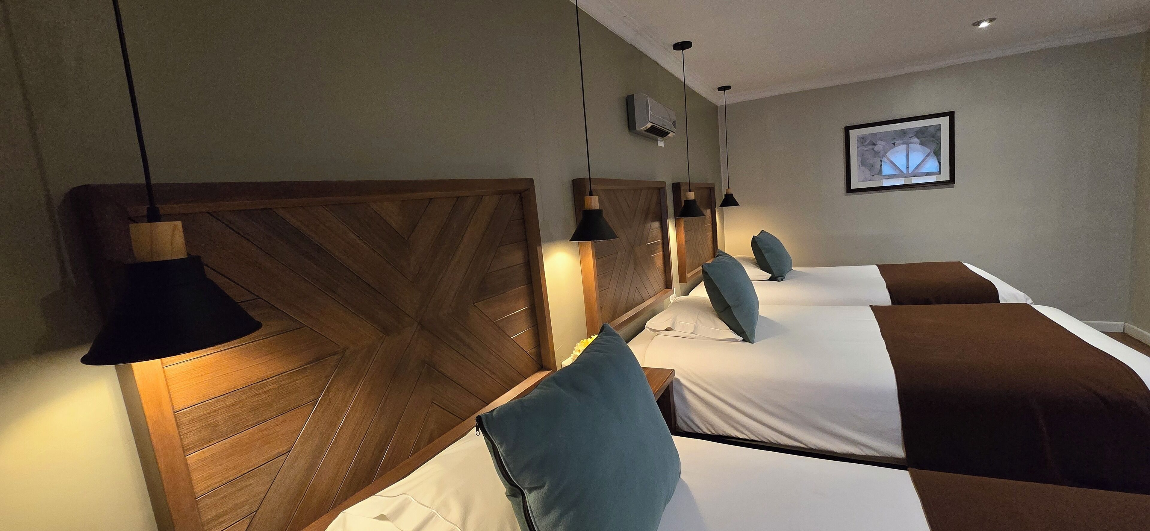 A hotel room with a wooden headboard, a bed with white and brown bedding, and a wall-mounted air conditioner.