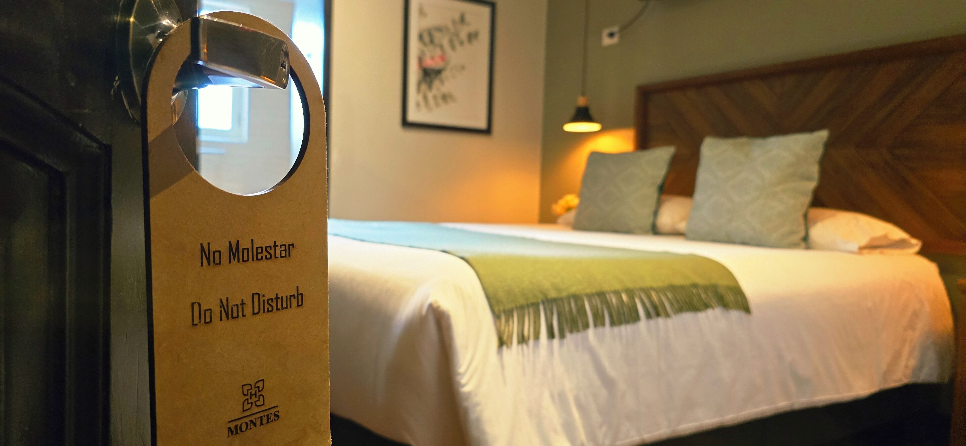 Ein Hotelzimmer mit Bett, Kopfteil, Wandbild und Tür mit Schild.