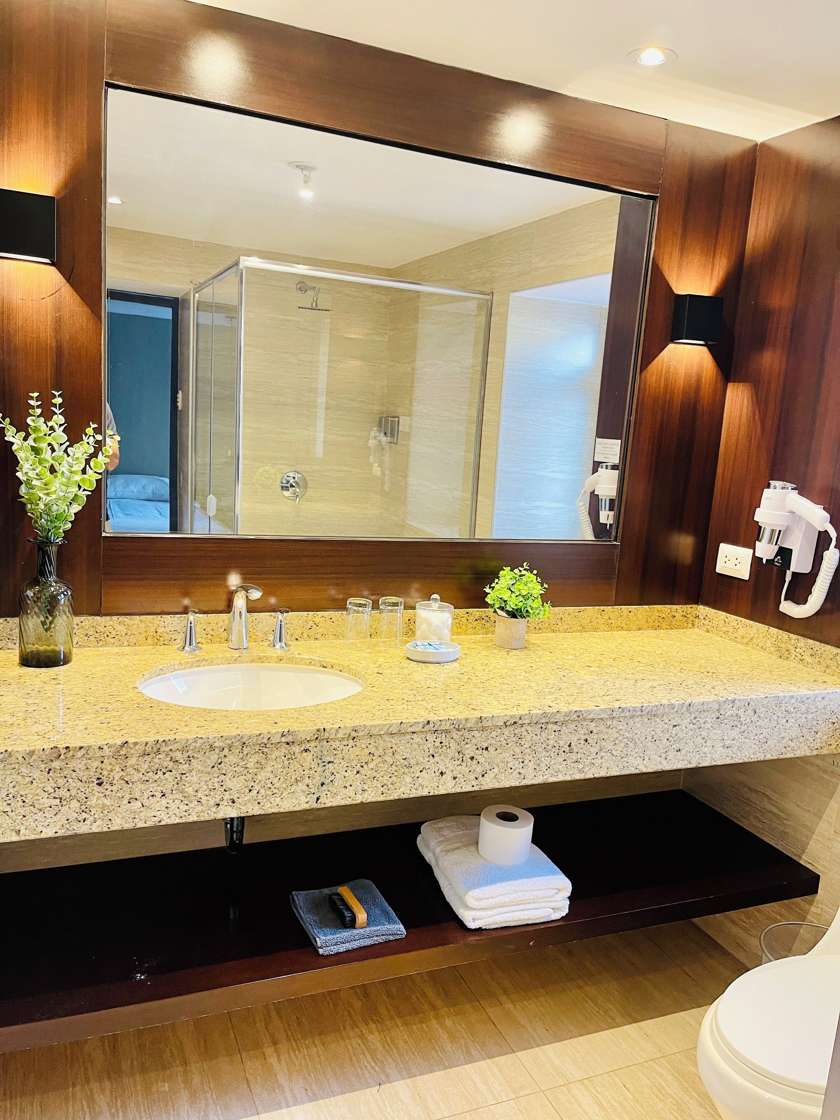 Une salle de bain avec un grand miroir, deux lavabos, une douche, un porte-serviettes et des toilettes.