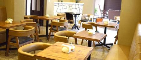 A cozy restaurant with wooden tables and chairs, a stone fireplace, and a comfortable seating area.