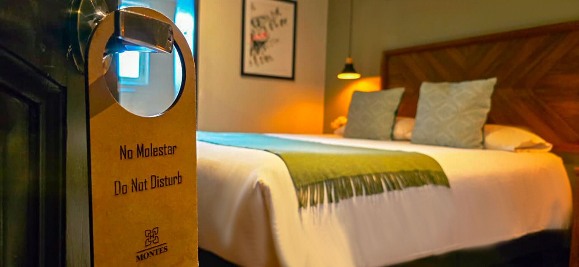 Quarto de hotel com uma cama, uma placa na porta e um quadro na parede.