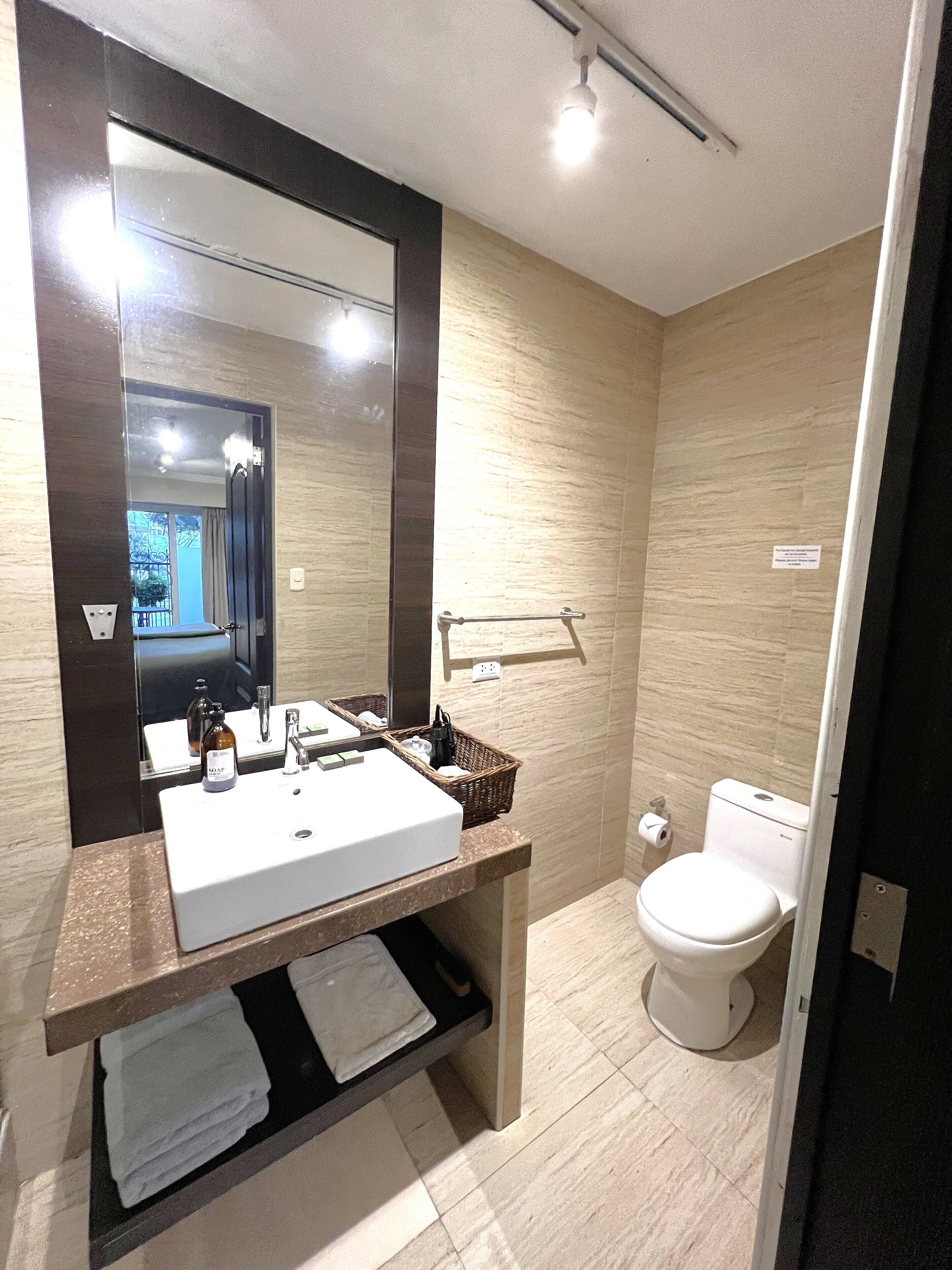 Baño con lavamanos, espejo e inodoro blancos.