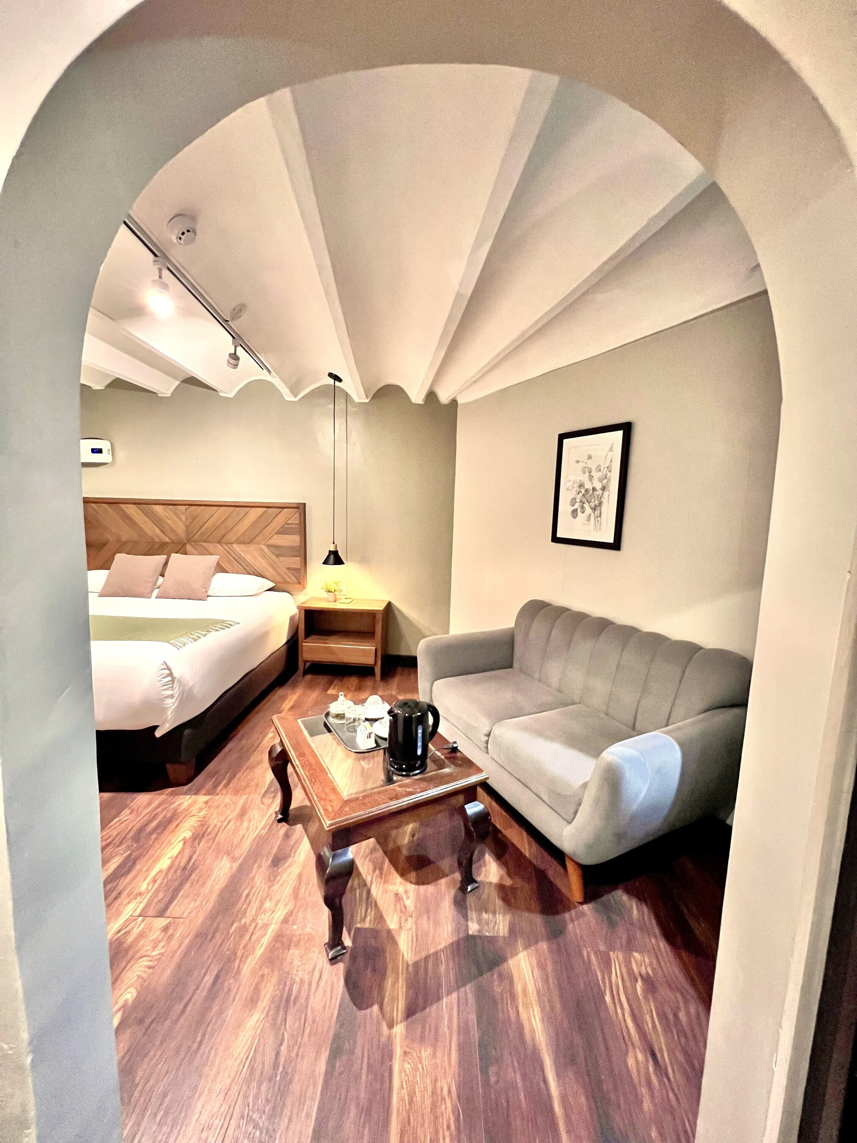 A compact hotel room with a bed, a sofa, a coffee table, and a nightstand.
