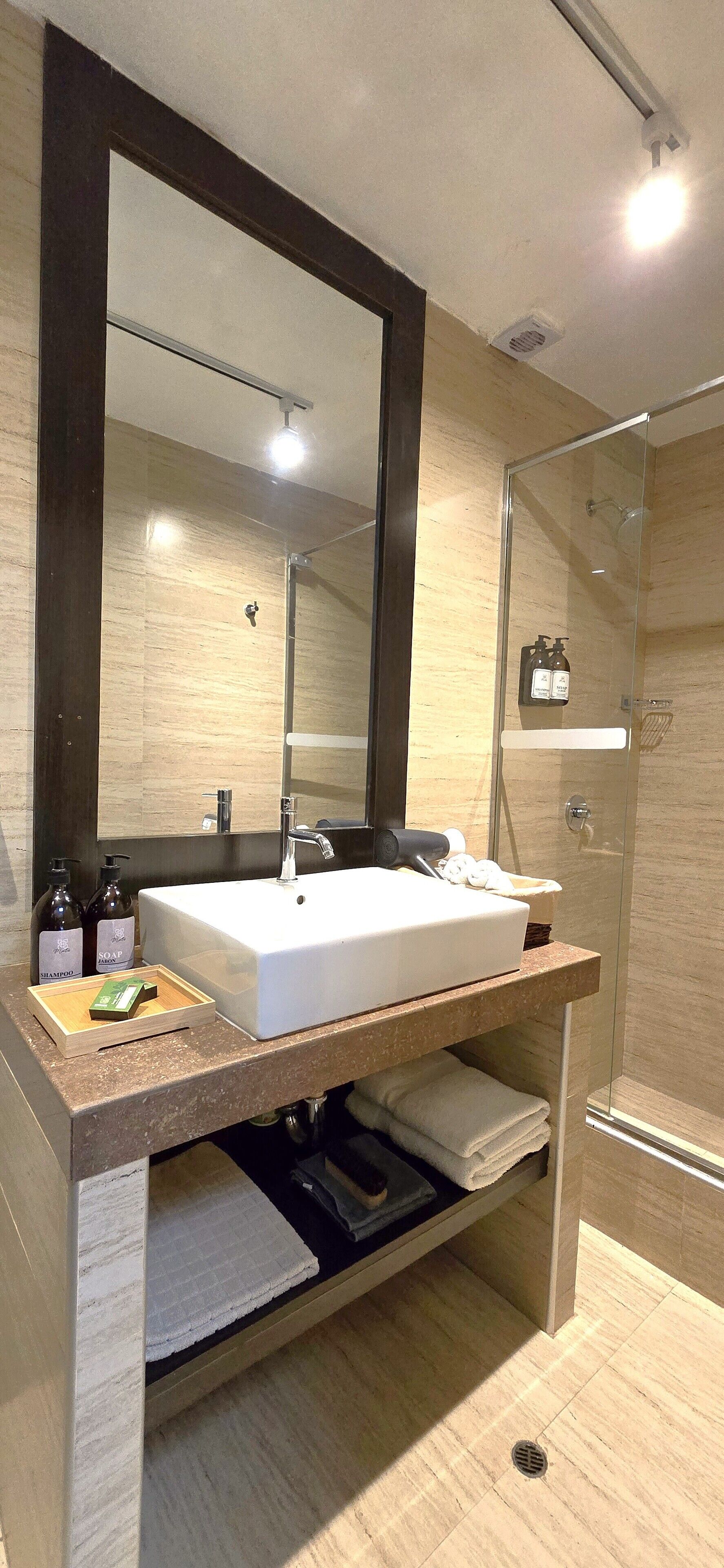 Un baño moderno con un espejo grande, un lavabo blanco y una ducha con cerramiento de vidrio.