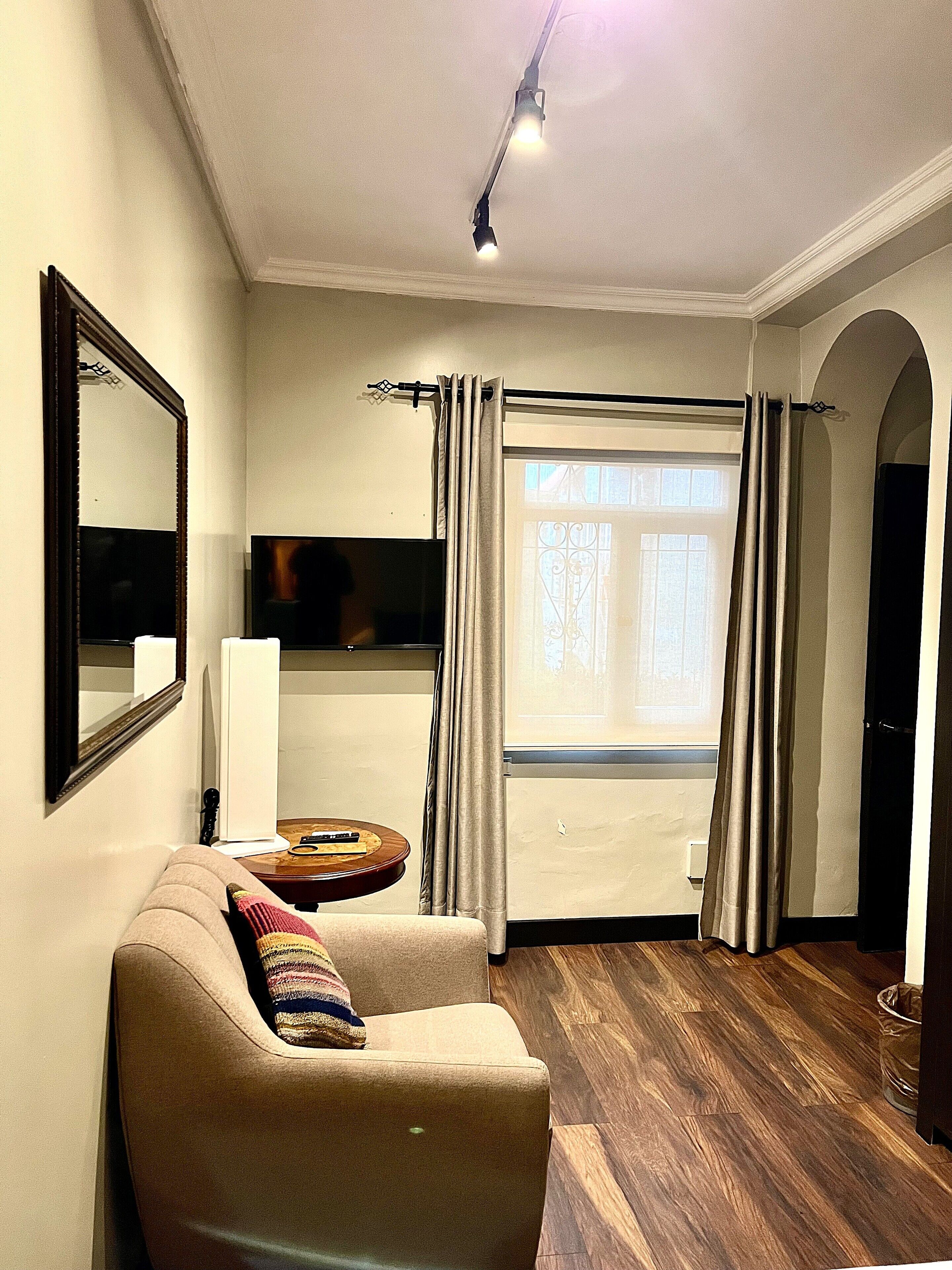 A living room with a sofa, a flat-screen TV, a window with curtains, and a ceiling light.