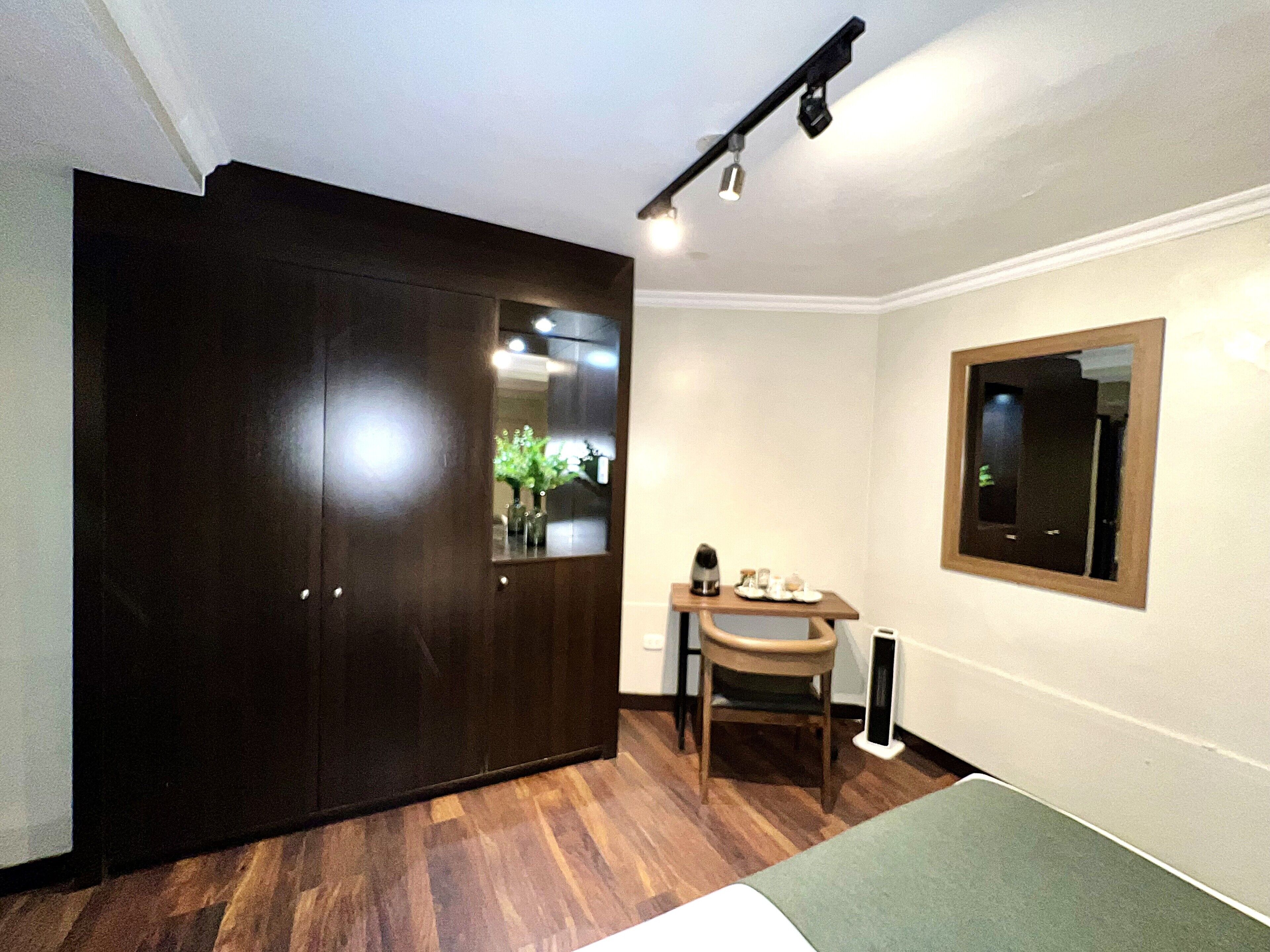A room with a wooden floor, a bed, a desk with a chair, a mirror, and a wardrobe.