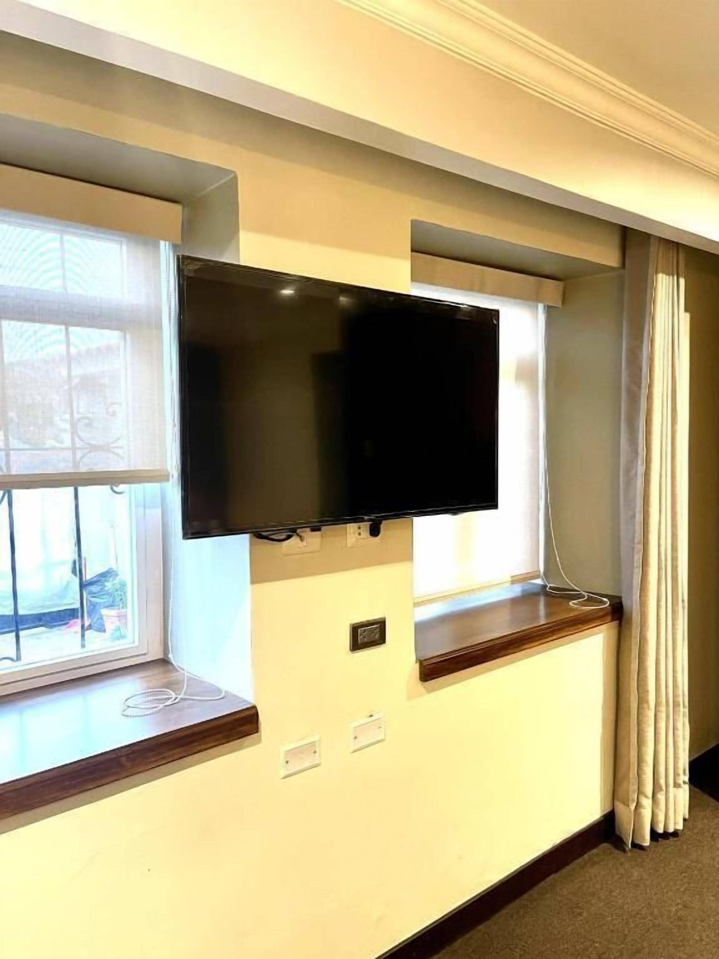 A room with a flat-screen TV mounted on the wall, a window with a curtain, and a wooden ledge.