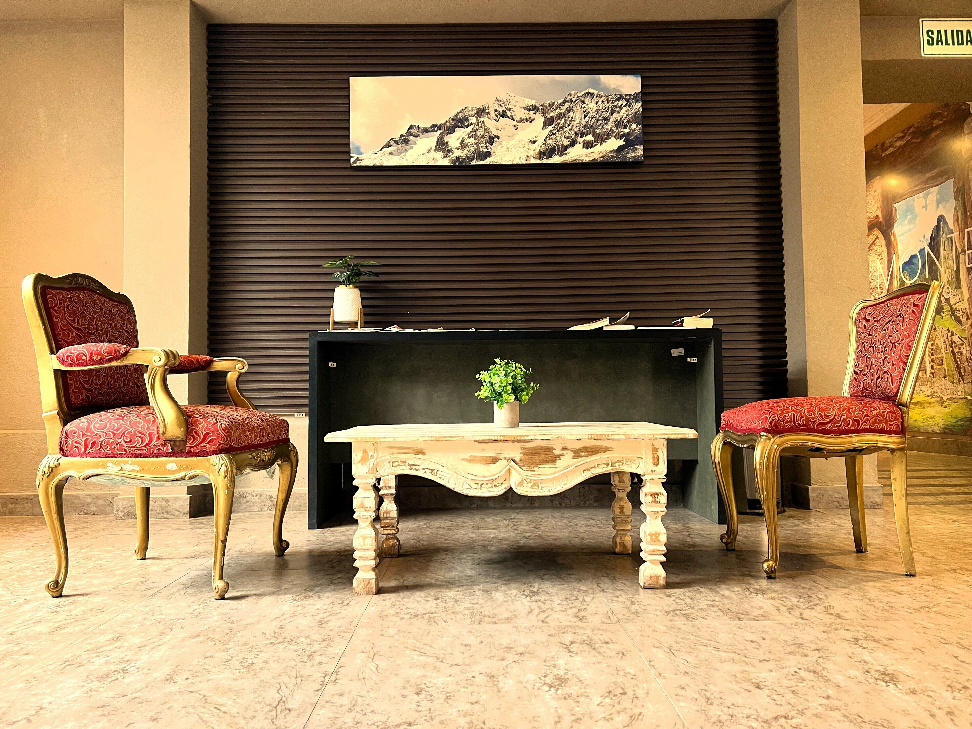 A lobby with two ornate chairs, a wooden table, a painting on the wall, and a sign that reads 'SALIDA'.