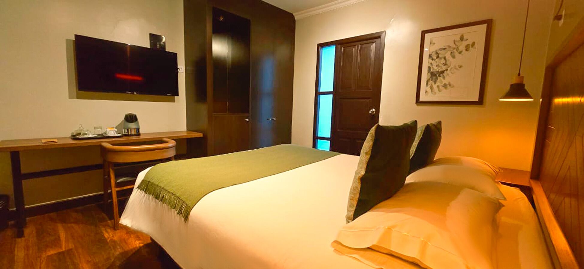 A hotel room with a bed, desk, chair, and a television on the wall.