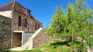 Un bâtiment en pierre avec un toit recouvert de tuiles rouges, un escalier menant à une porte et un arbre au premier plan.