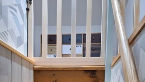 Un escalier en bois, doté d’une rampe, mène à une pièce avec une fenêtre et une porte.