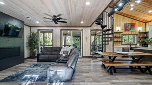 A spacious living area with a large sectional sofa, a ceiling fan, and a wooden dining table with benches. - Broken Bow Cabin with Hot Tub and Game Room (Broken Bow)