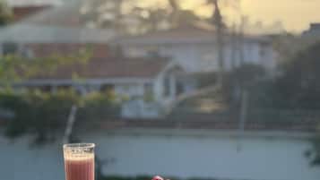 Un bicchiere di smoothie e un piatto di lamponi su un balcone con vista sul tramonto.
