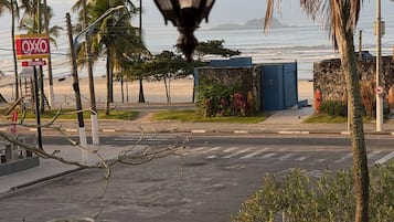Vista da praia com um poste de luz, palmeiras e uma placa da 'Oxxo'.
