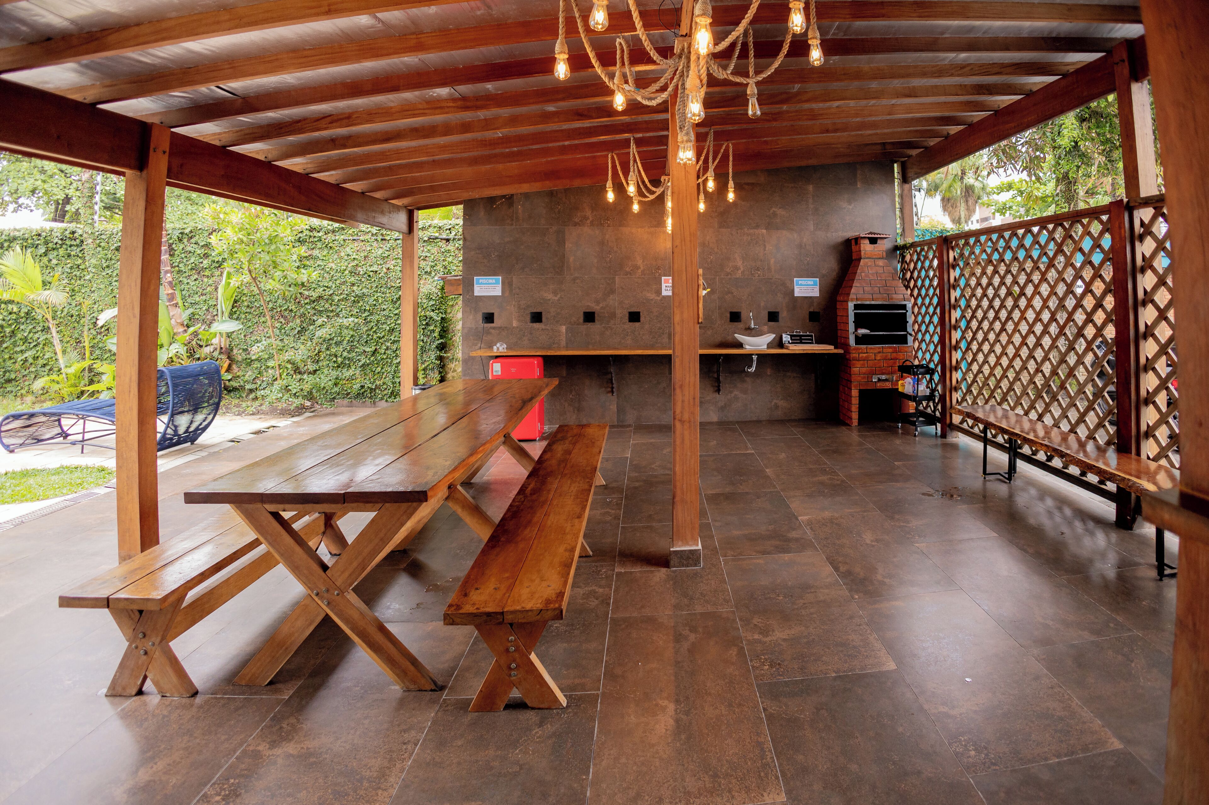 An outdoor patio with wooden benches, a brick oven, and a lattice fence.