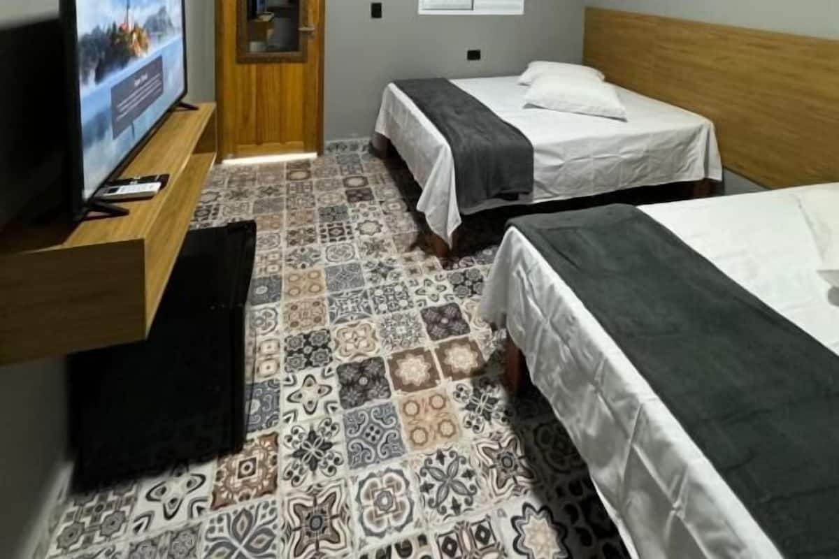 Ein Zimmer mit zwei Betten, einem Fernseher, einer Holztür und einer Klimaanlage.