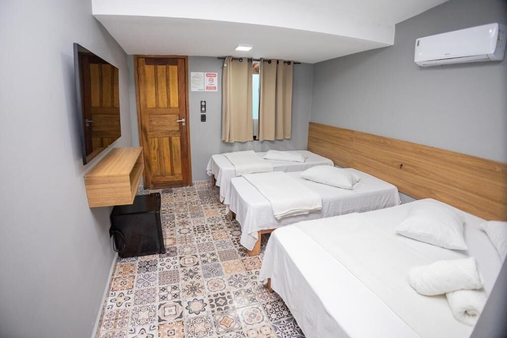 A hotel room with three beds, a wooden headboard, a flat-screen TV, a minibar, and a tiled floor.