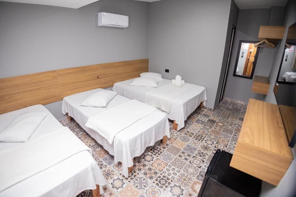A hotel room with three beds, a wooden headboard, a patterned floor, a small desk, and a mirror.