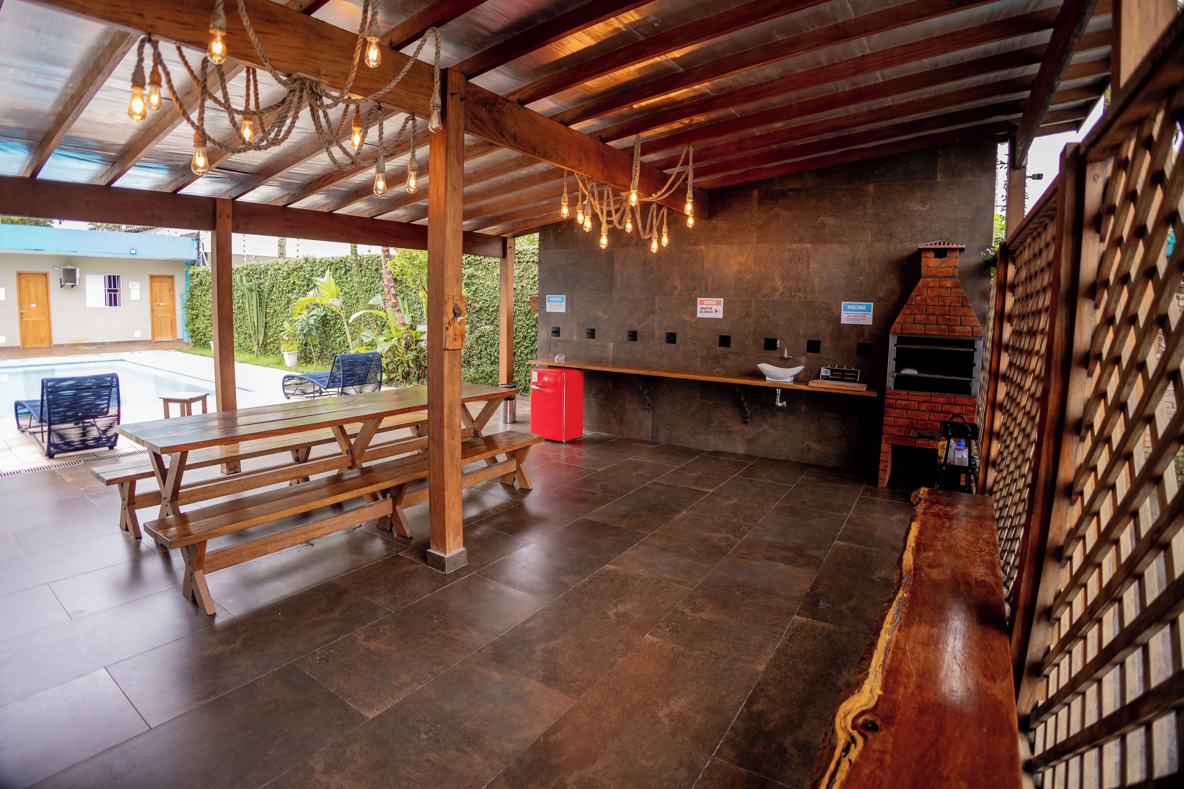 A covered outdoor area with wooden benches, a red cooler, and a brick oven.