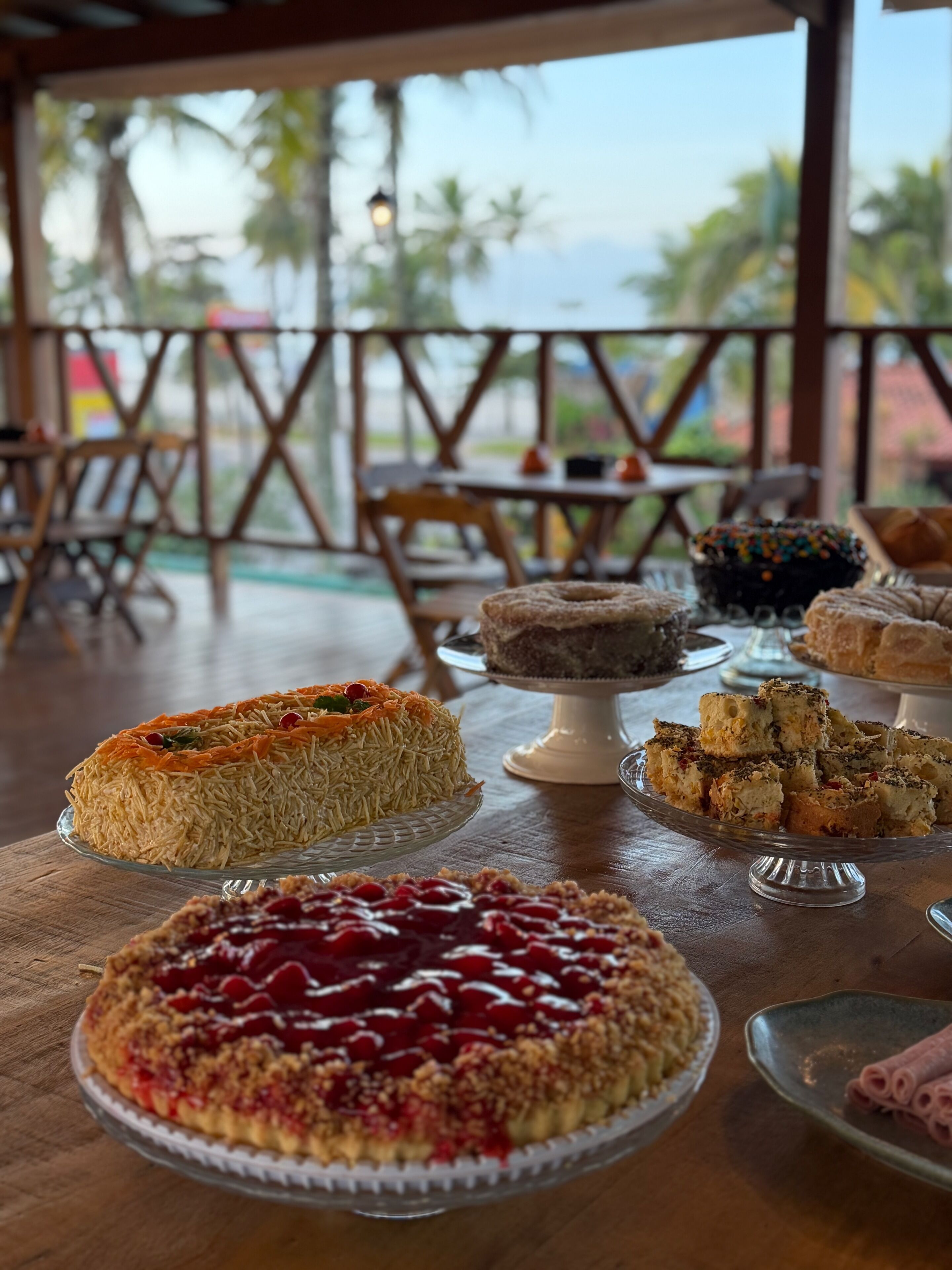 Diversos postres sobre una mesa en un comedor con vista a palmeras.