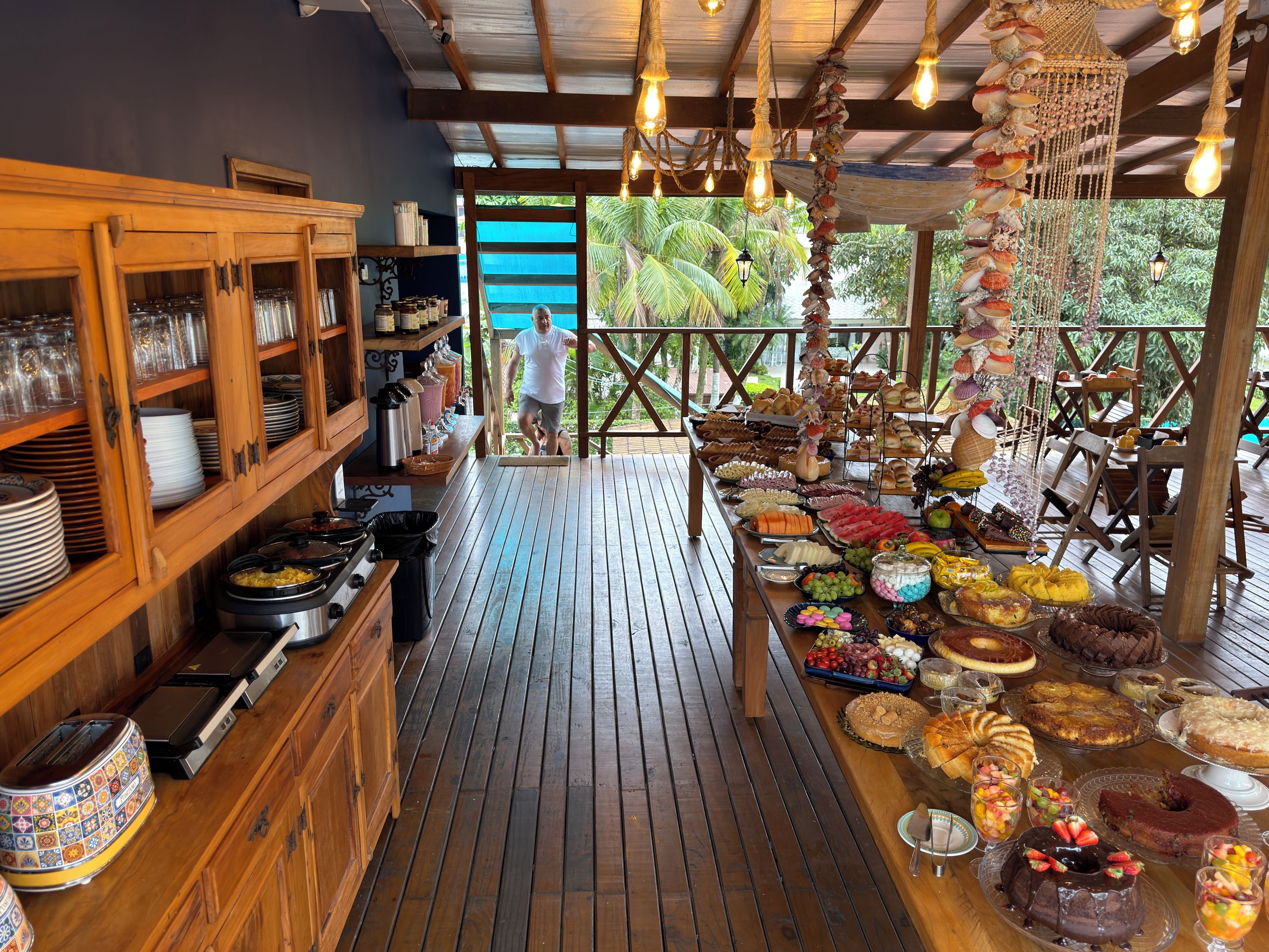 A covered outdoor dining area with a variety of food and drink options, wooden furniture, and a view of the outdoors.
