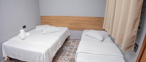 A hotel room with two single beds, a wooden headboard, a patterned floor, and a wall-mounted air conditioner.