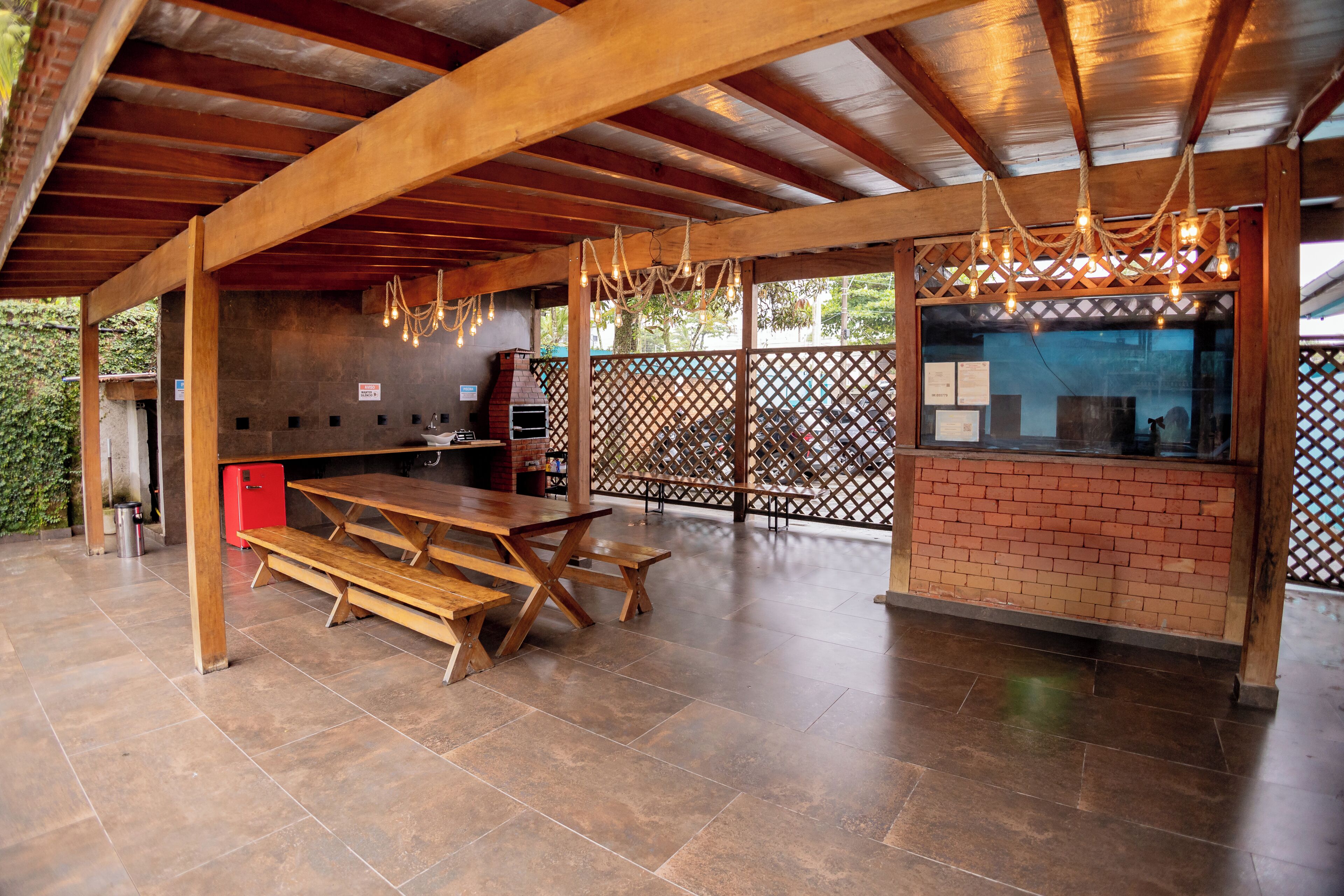 An outdoor patio with a brick barbecue area, wooden benches, and a wooden ceiling structure.