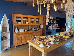 A wooden buffet table with various desserts and a wooden cabinet with glassware. - Santa Clara Pousada (Guarujá)