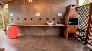 A covered outdoor area with a brick oven, a sink, and a red refrigerator. - Santa Clara Pousada (Guarujá)
