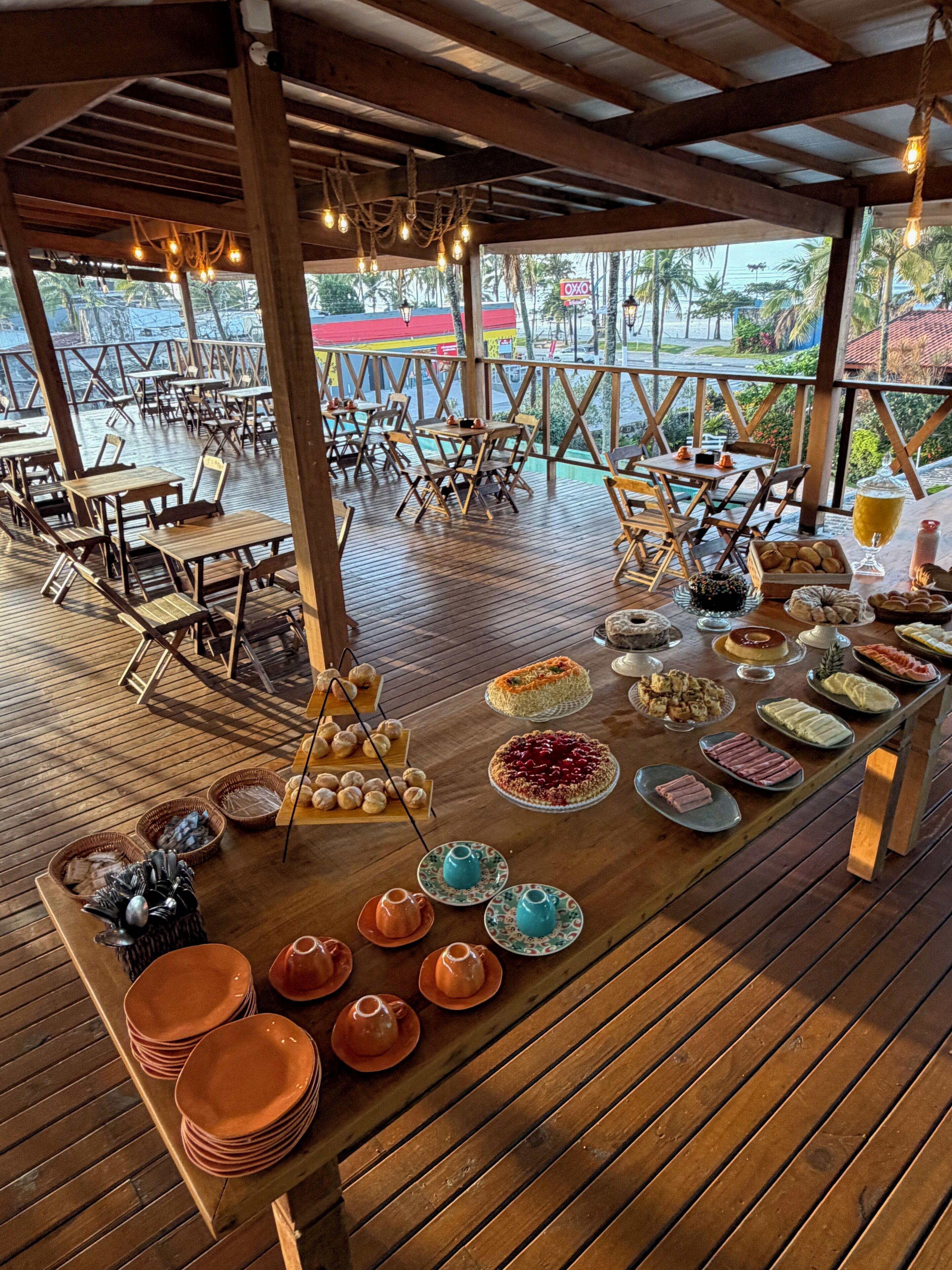 Un área de comedor al aire libre con mesas y sillas de madera, un bufé con diversos platos y vistas del paisaje circundante.