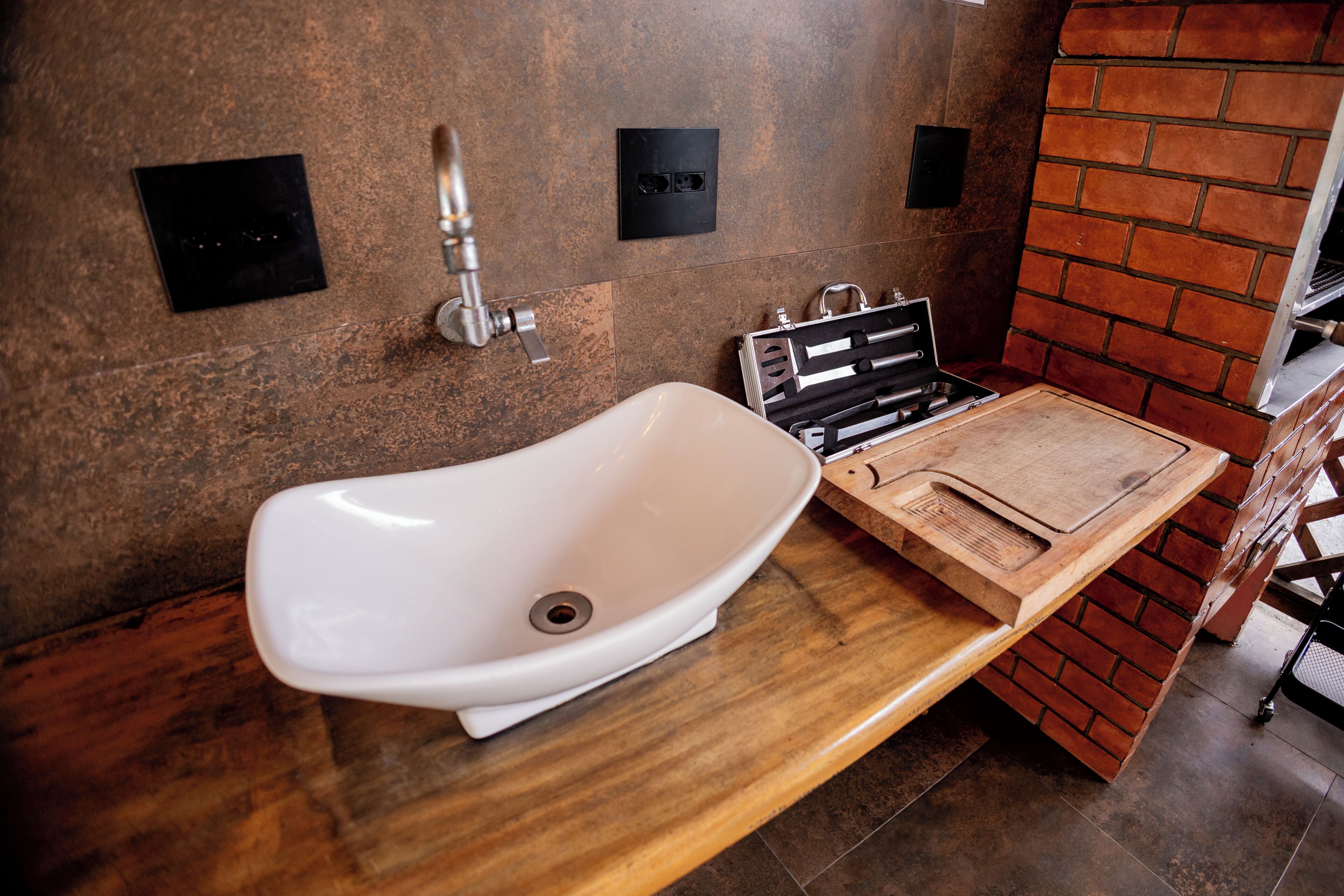 A bathroom with a white sink, a wooden vanity, and a brick accent wall.