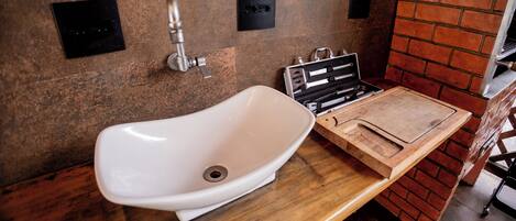 A bathroom with a white sink, a wooden vanity, and a brick accent wall.