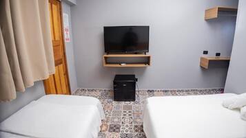 Ett hotellrum med två sängar, en tv på ett träställ, en liten svart högtalare och ett klinkergolv.