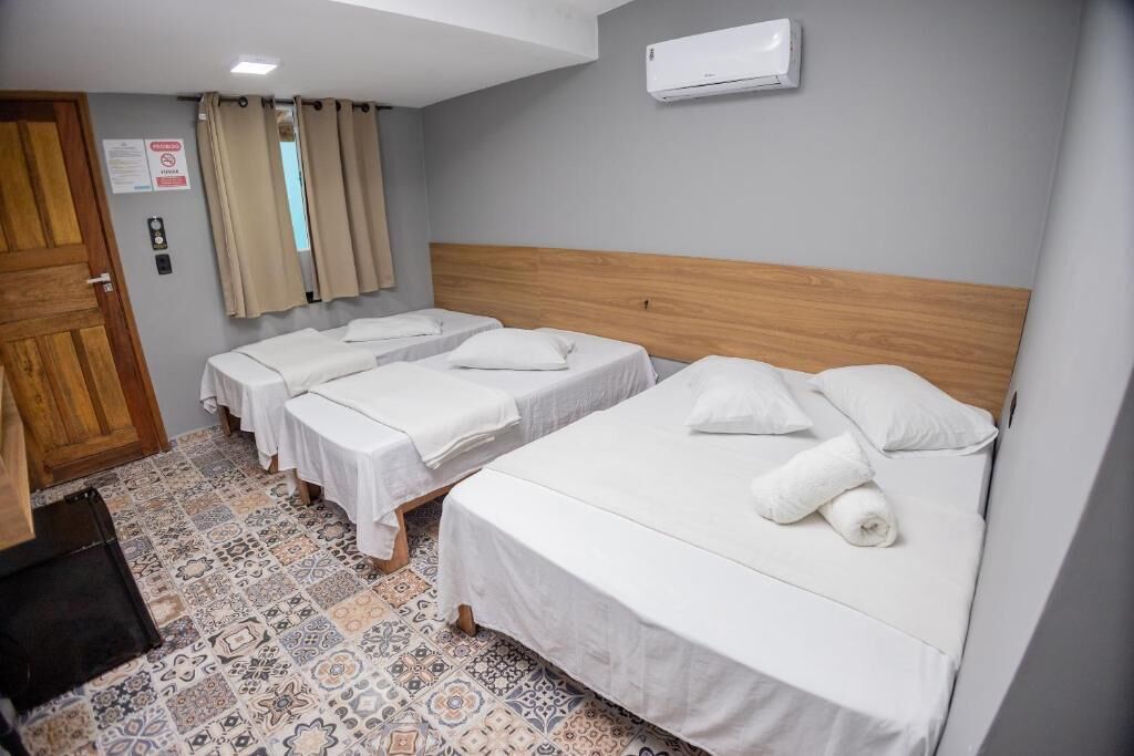 Een hotelkamer met drie enkele bedden, een houten hoofdeinde, een betegelde vloer en een raam met gordijnen.