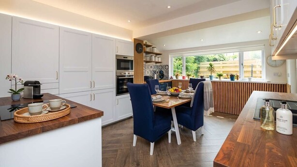 A modern kitchen with white cabinets, a dining area with blue chairs, and a view of greenery outside. - 3BR Peebles Home - Free Parking - Near Glentress (Peebles)