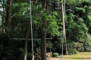 A wooden swing set in a wooded area with a stack of logs nearby. - Strandvilla Hubertus - H4 - Claude Monet (Ostseebad Boltenhagen)