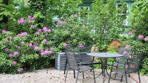 Un jardin avec une table et des chaises, entouré de verdure et de fleurs roses.