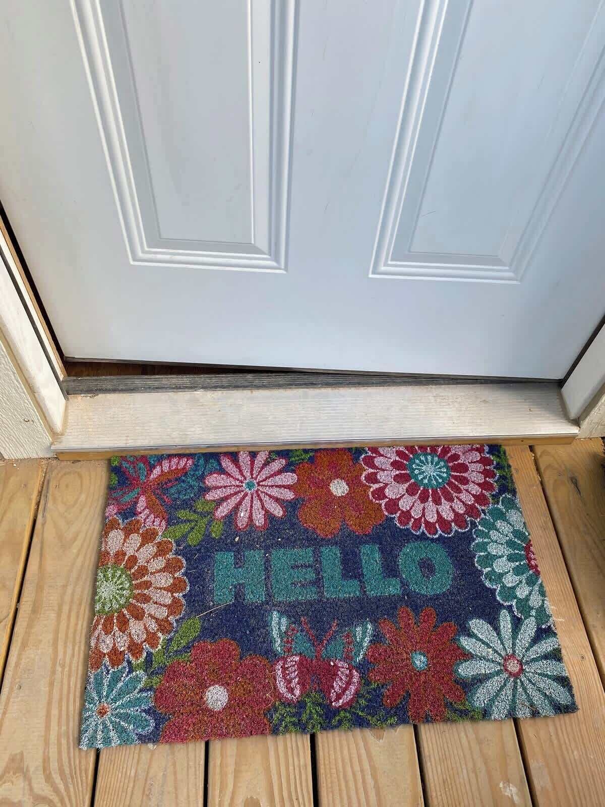 Een kleurrijke deurmat met bloemmotieven en de tekst 'HELLO' op een houten dorpel.