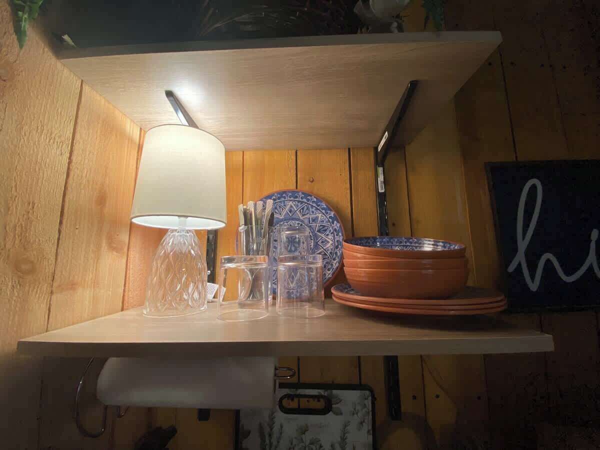 A wooden shelf with a white lamp, clear glasses, and a blue and white patterned bowl.