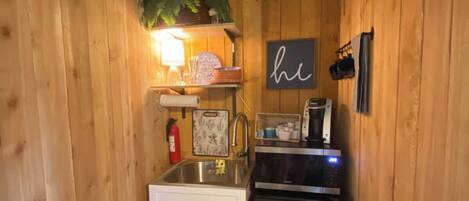 A compact kitchen with wooden walls, a sink, a stove, and a microwave.