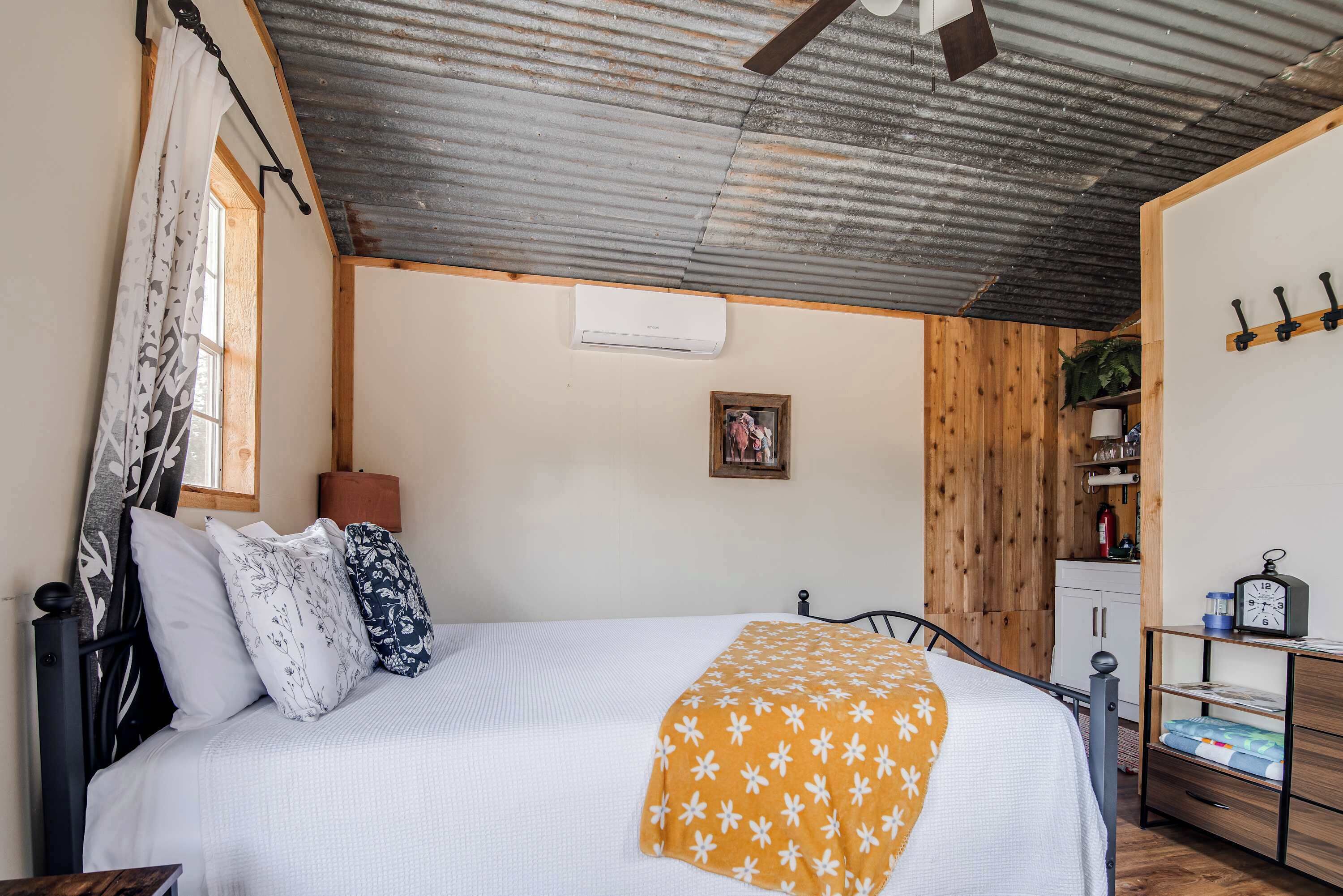 Une chambre à coucher comprenant un lit, une armoire en bois, une table de chevet et un climatiseur fixé au mur.
