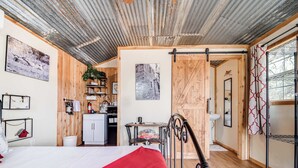 A compact room with a bed, a small kitchenette, a bathroom, and a view of the outdoors. - Hill Country Cabin 4 | Cozy Couples Retreat (Canyon Lake)