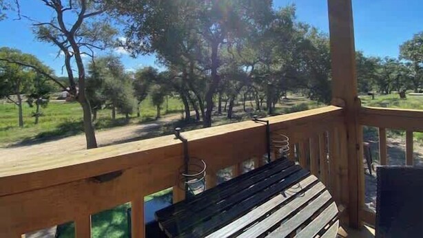 A wooden deck with a bench, overlooking a grassy area with trees. - Hill Country Cabin 4 | Cozy Couples Retreat (Canyon Lake)